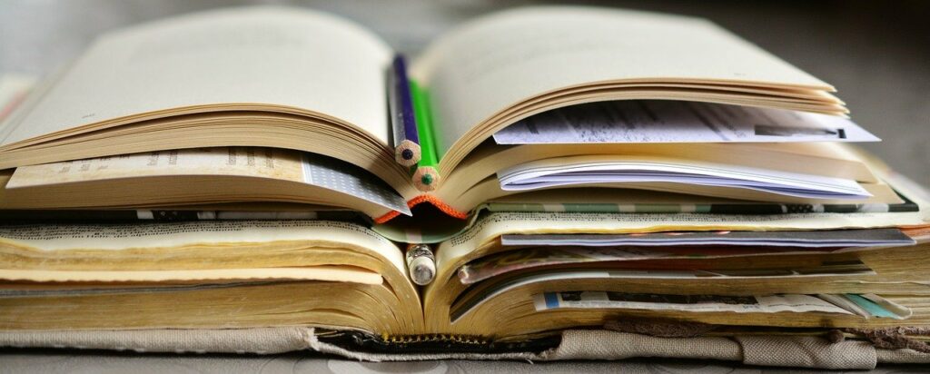 mehrere aufgeklappte Bücher übereinandergestapelt, teilweise mit eingelegten Stiften